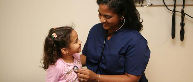 在例行检查中，一位医疗保健专业人员用听诊器轻轻地检查一个微笑的小孩.
