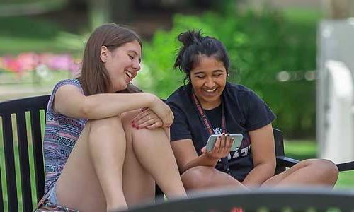 two Carroll University students looking at a phone and laughing.